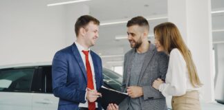 Uśmiechnięta para odbiera nowy samochód od sprzedawcy w salonie
